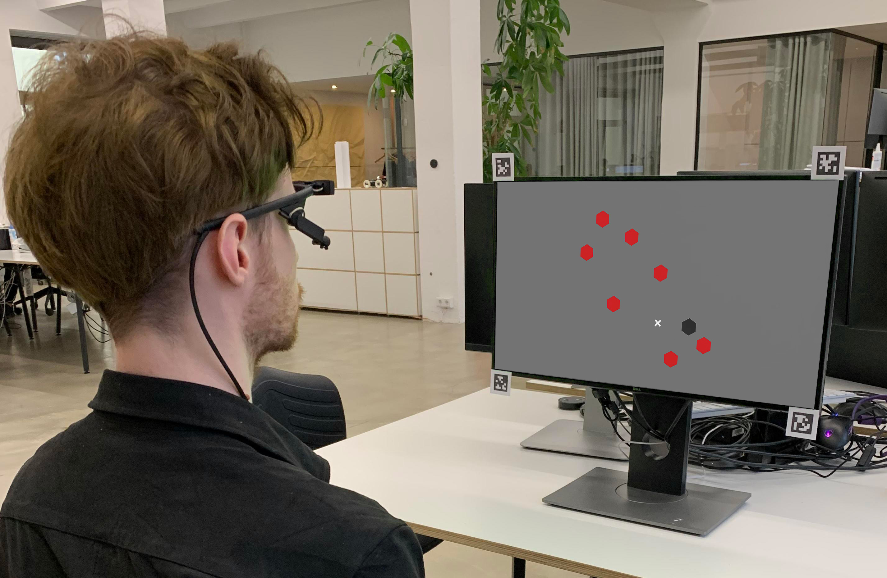 Subject wearing Pupil Core headset, looking at a Computer screen setup with AprilTag markers