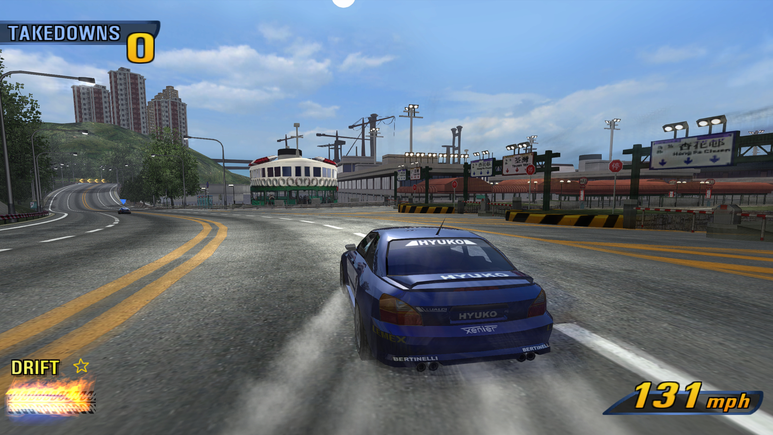 A blue car drifting at 131 mph on a sunny harbour road in the Far East, a ferry and tower blocks behind