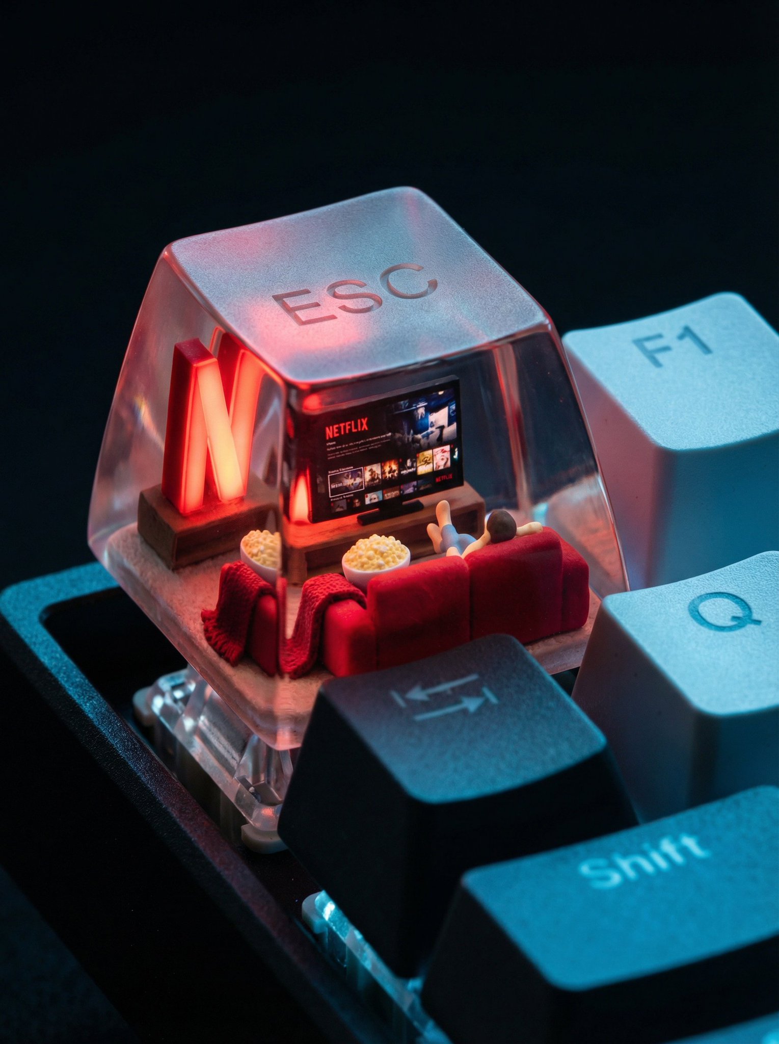 A photorealistic ESC keycap scene shows a miniature cozy living room setup. Inside: a glowing red Netflix screen, a p…
