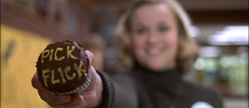 Still frame from the movie Election, the character Tracy Flick is holding up a cupcake with the lettering "Pick Flick" across the icing.